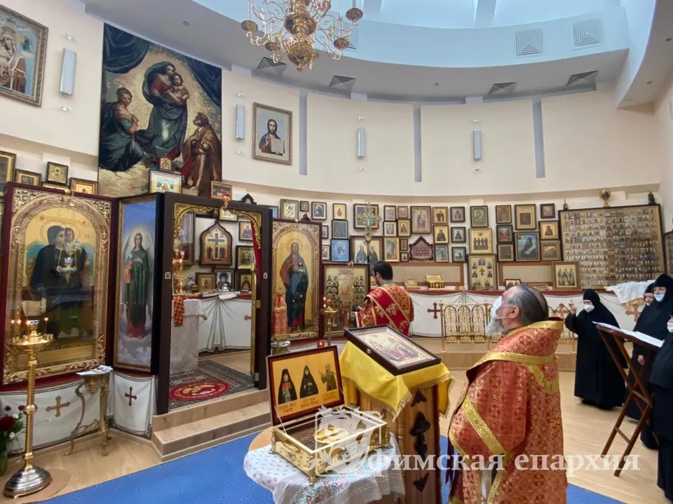 Круглый зал домового храма: митрополит Никон совершает литургию перед аркой с иконостасом, стены до потолка увешаны иконами, наверху — образ Покрова Богородицы